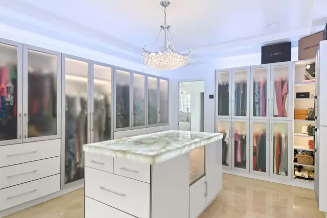 Custom walk-in closet in Orlando with frosted glass-front wardrobes, a stone-topped island and a crystal chandelier