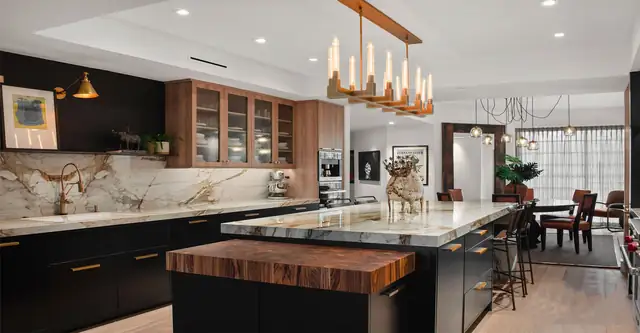 Modern kitchen with black lower cabinets, butcher-block island, marble slab backsplash and a linear brass chandelier
