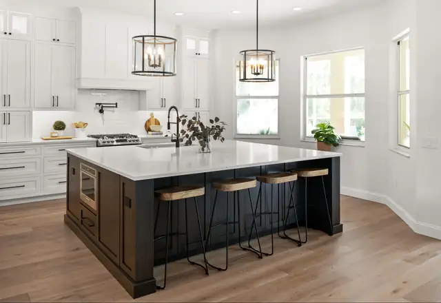 White kitchen with a black island, quartz counters, woven counter stools and two black lantern pendants