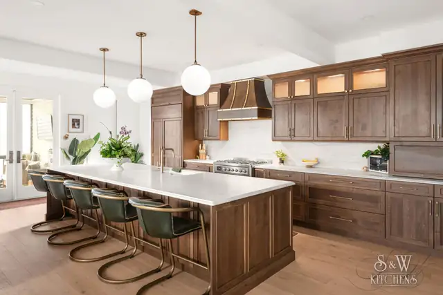 Kitchen with walnut shaker cabinets, copper range hood, lit glass uppers and a long white island with green stools