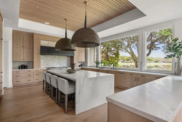 Whole-house remodel kitchen with white oak cabinets, marble waterfall island and woven pendant lights facing a lake view