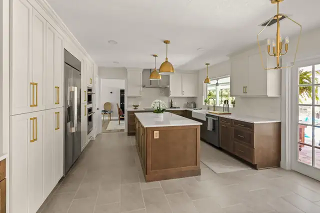 White and walnut kitchen with brass pendants, a tall pantry wall and a center island